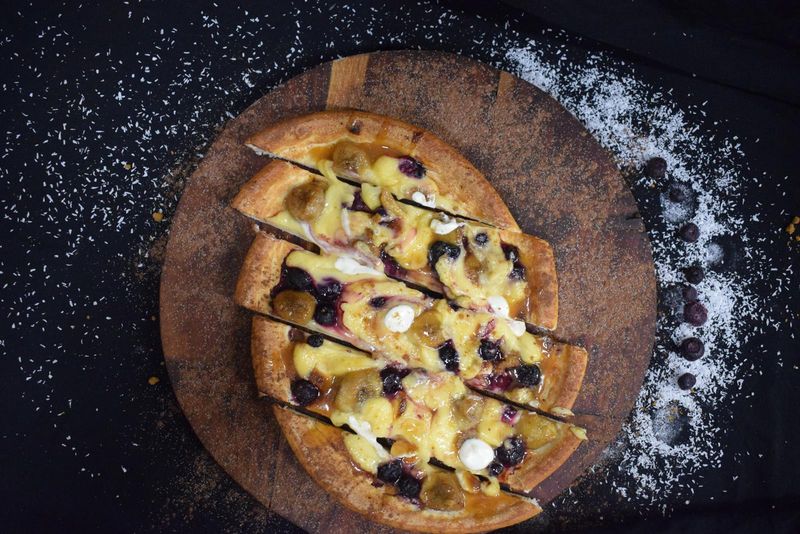 Sliced dessert pizza with blueberries and custard on a wooden board